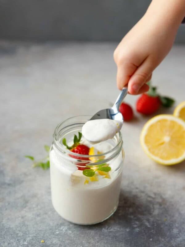 A jar filled with lemon cottage cheese mousse and a hand holding a spoon over it.