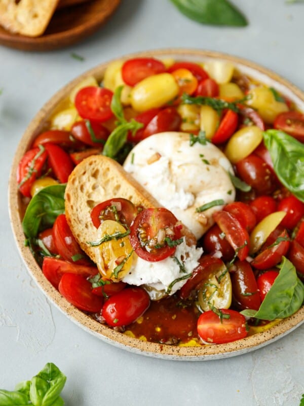 A plate with marinated grape tomatoes, Burrata cheese and a slice of crusty bread.
