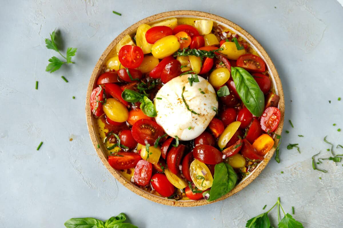 A round plate with colorful marinated grape tomatoes and burrata cheese in the middle.