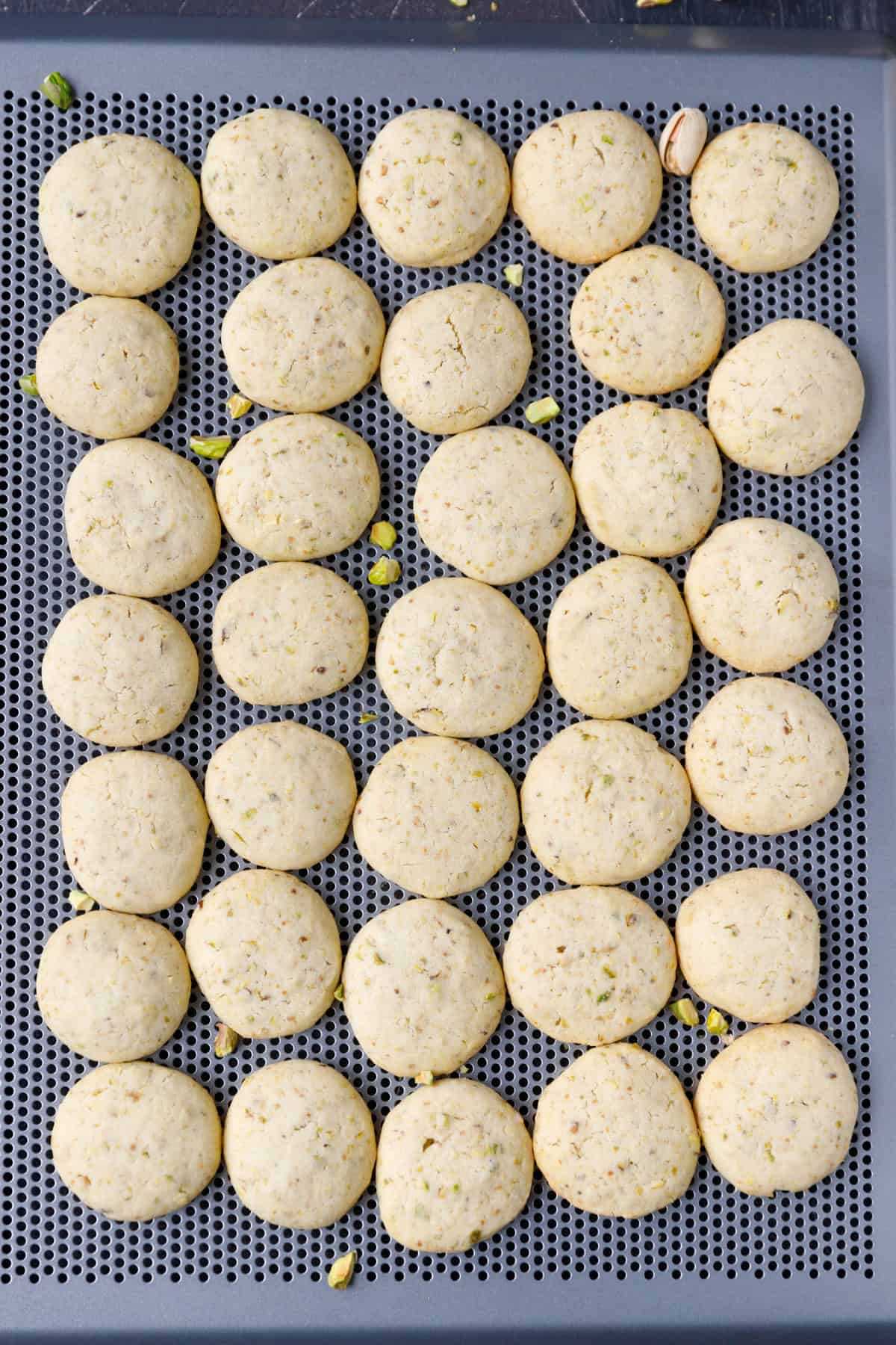 Baked pistachio cookies on a baking sheet before being filled with pistachio cream