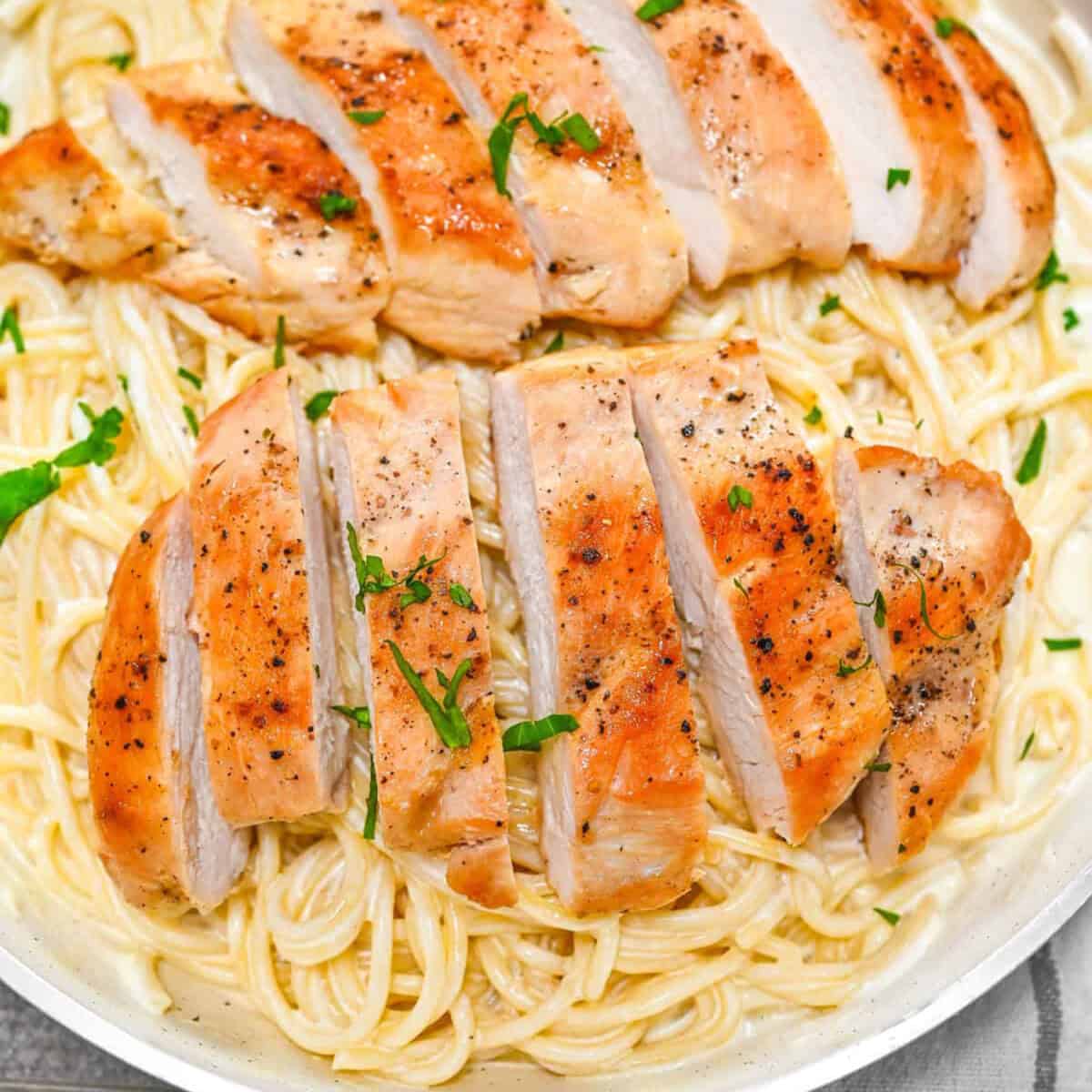 A skillet with garlic Parmean chicken pasta and sliced golden brown chicken breast