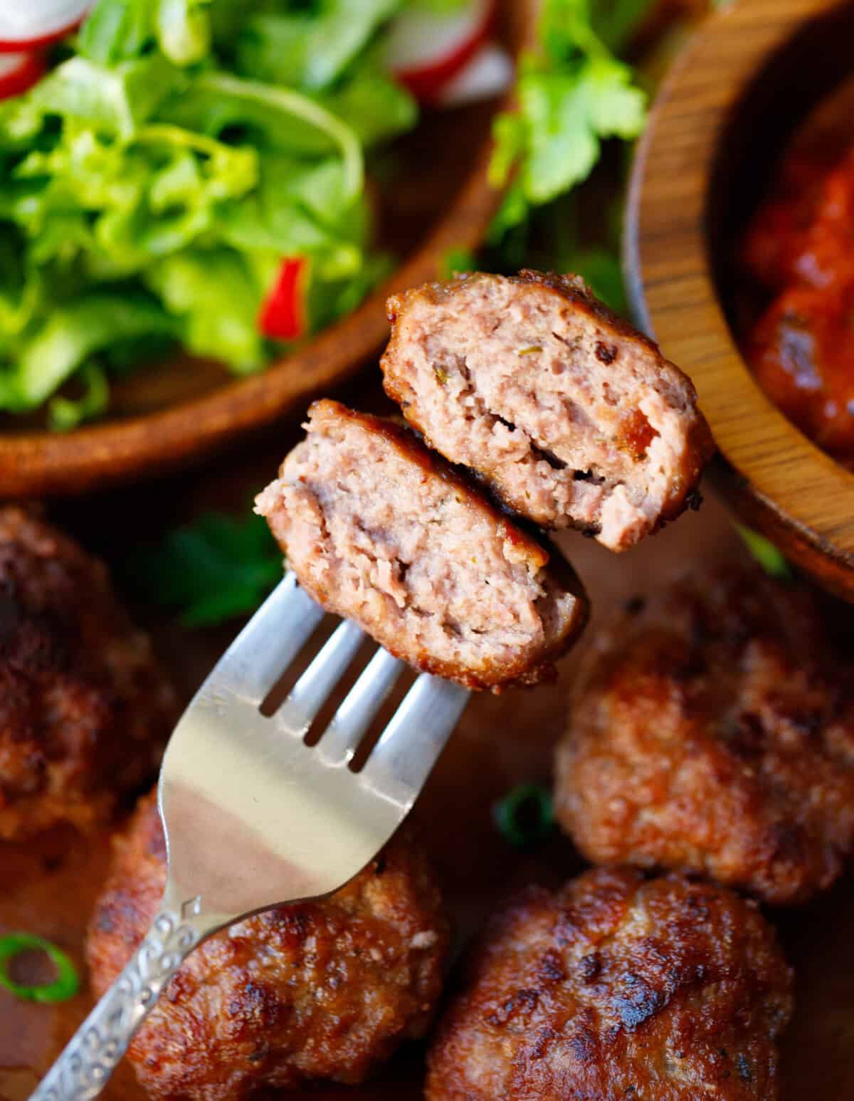 Fork holding a sliced Bulgarian-style beef meatball, showing the juicy interior and crisp crust.