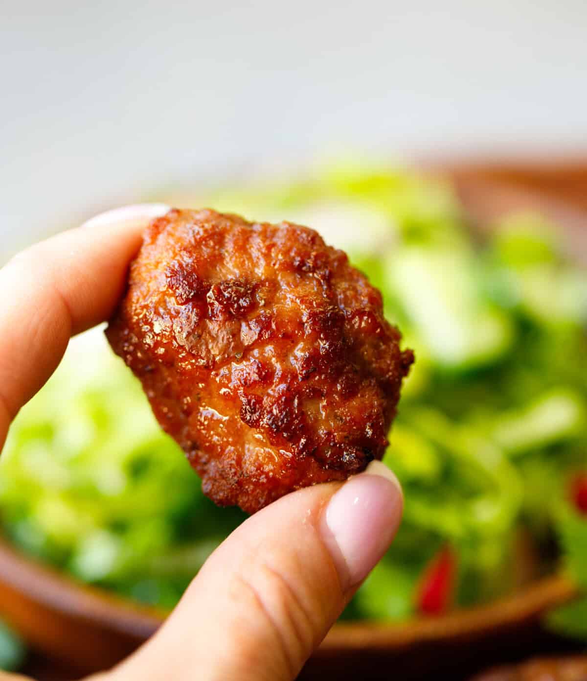 A hand holding a golden brown beef meatball.
