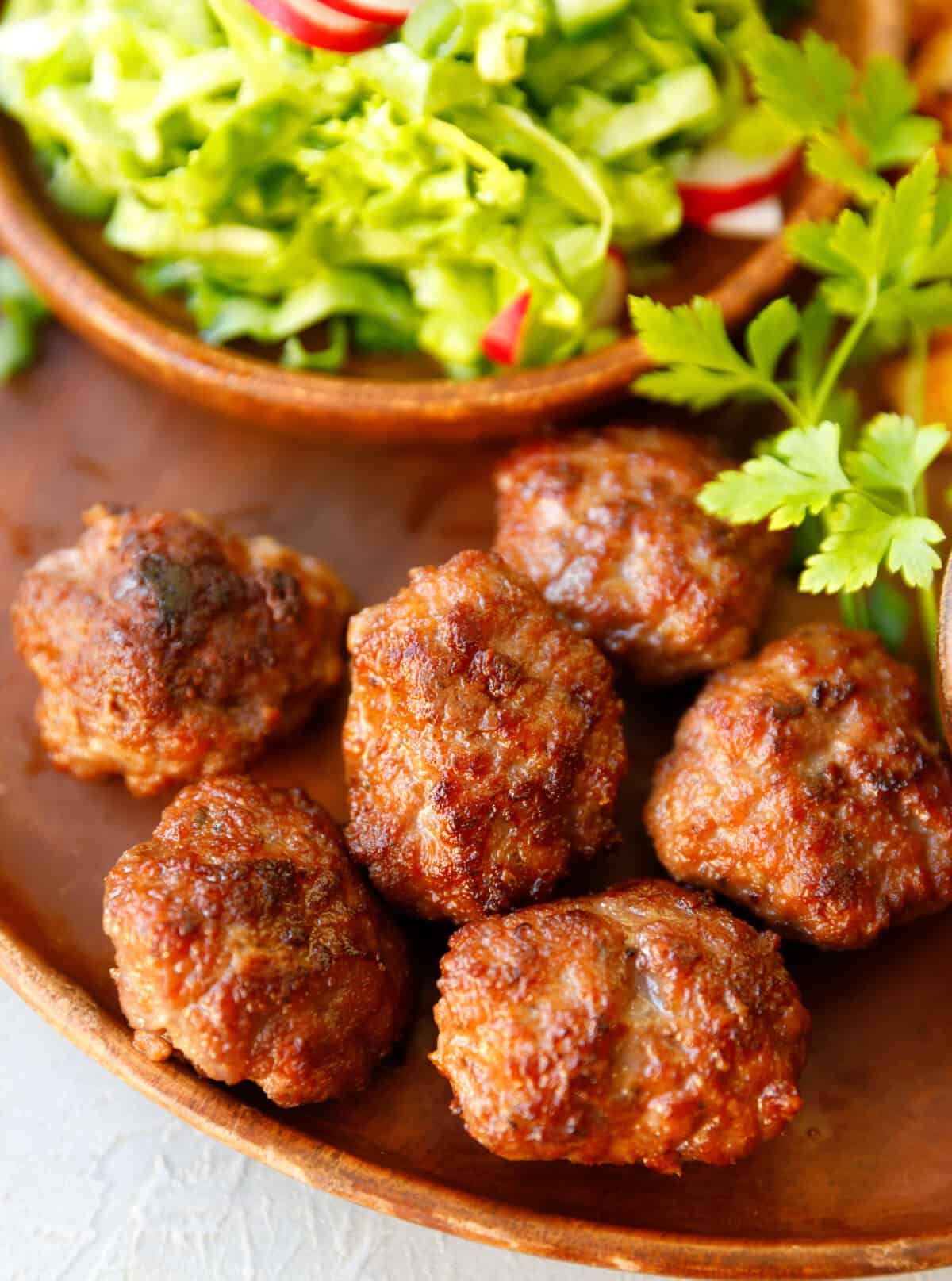 A wooden plate with juicy beef meatballs, and green salad
