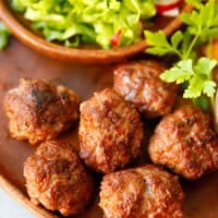 A wooden plate with juicy beef meatballs, and green salad