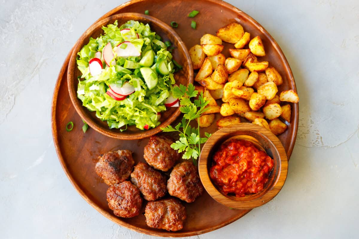 Full dinner plate with fried beef meatballs, roasted potatoes, cucumber salad, and tomato pepper dip