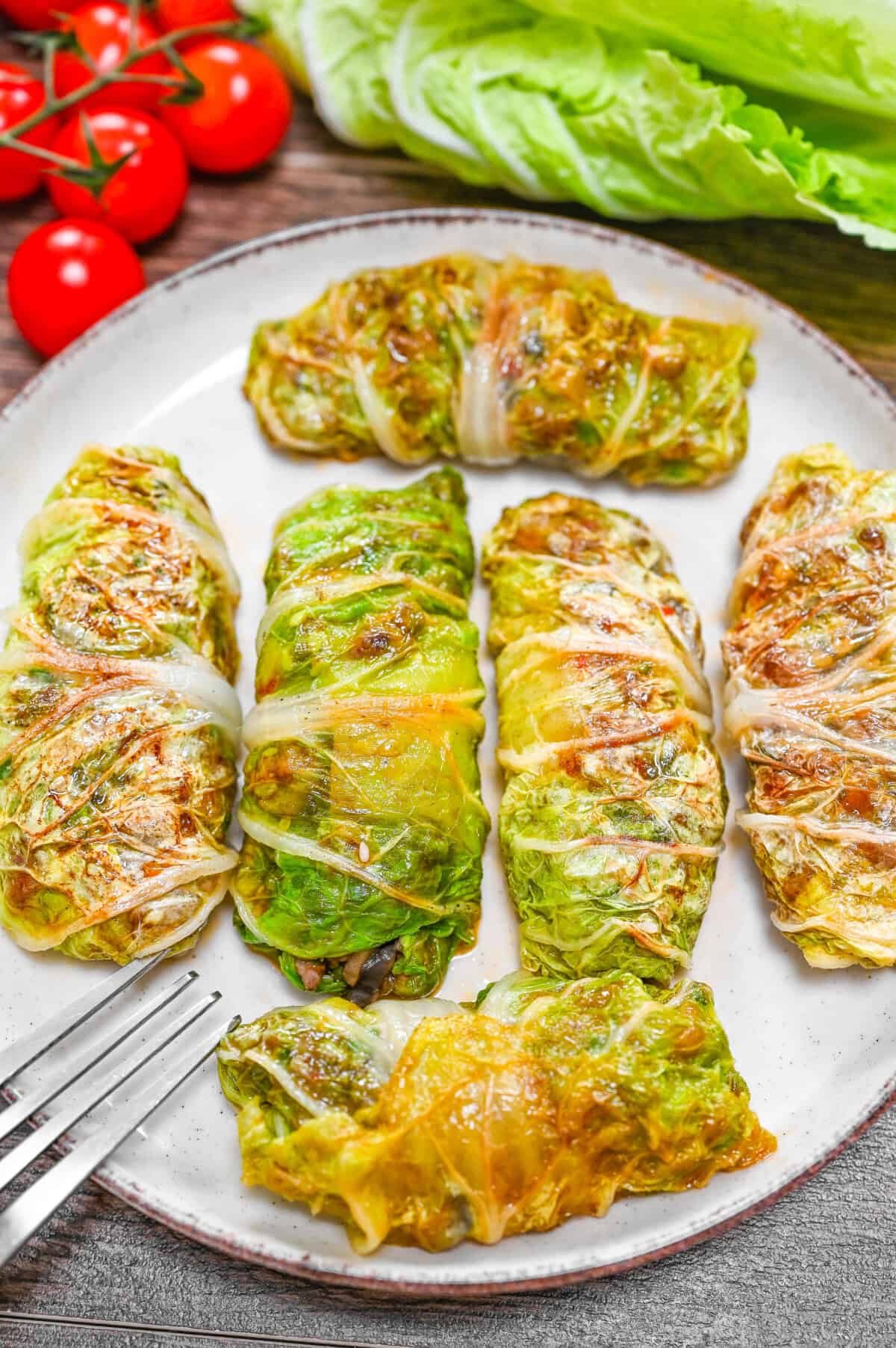 Golden pan-seared napa cabbage rolls stuffed with ground beef and mushrooms, drizzled with a savory soy-based sauce and sprinkled with sesame seeds and green onions.