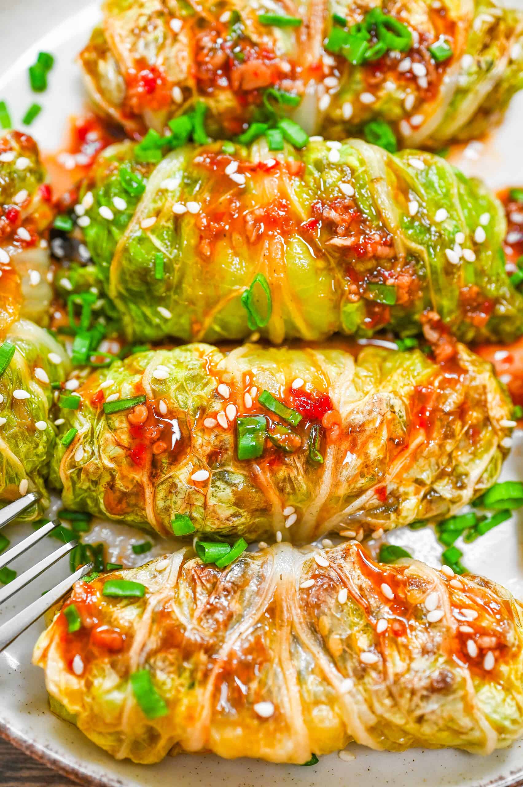 Close-up of seared napa cabbage rolls drizzled with a gingery soy-based sauce and garnished with scallions and sesame seeds.