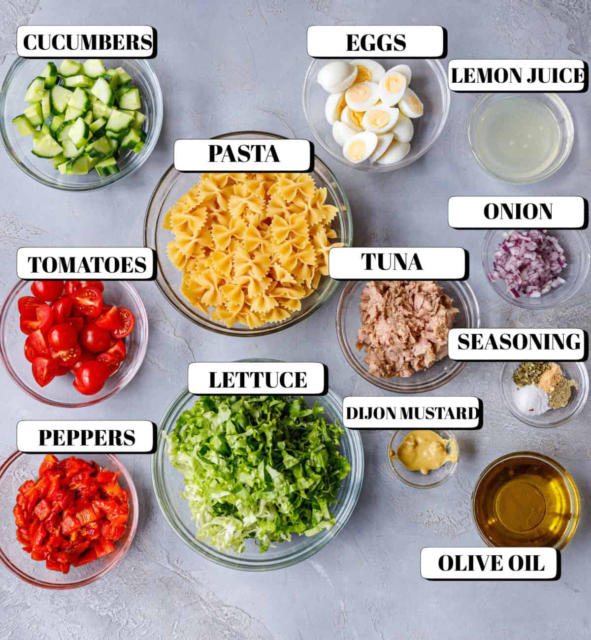 Flat lay of prepared ingredients for tuna pasta salad – bowtie pasta, tuna, eggs, cucumbers, tomatoes, and dressing components.