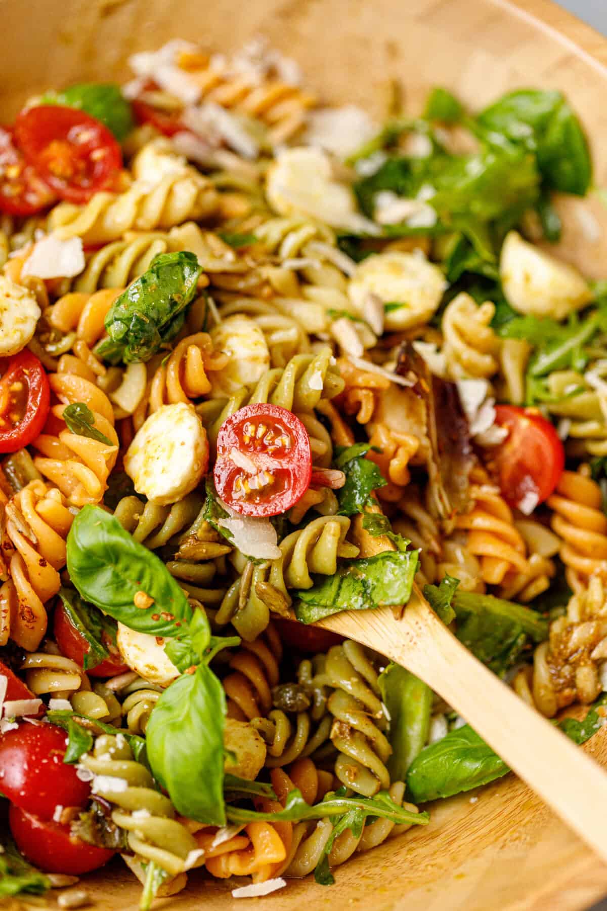 Tricolor fusilli pasta salad with fresh mozzarella, cherry tomatoes, greens, and sunflower seeds tossed in pesto dressing.