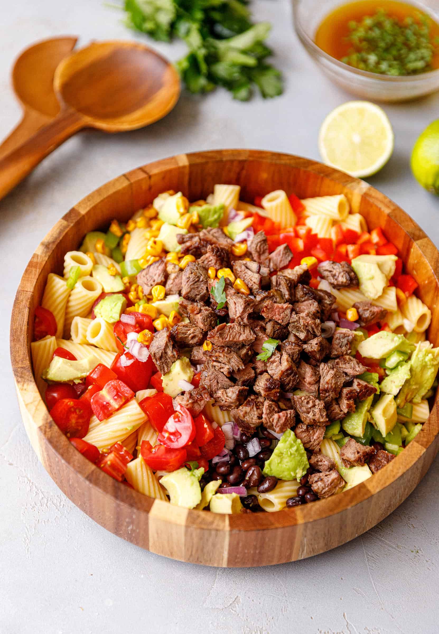 Overhead shot of steak pasta salad with corn, tomatoes, avocado, and rigatoni in a wooden bowl.
