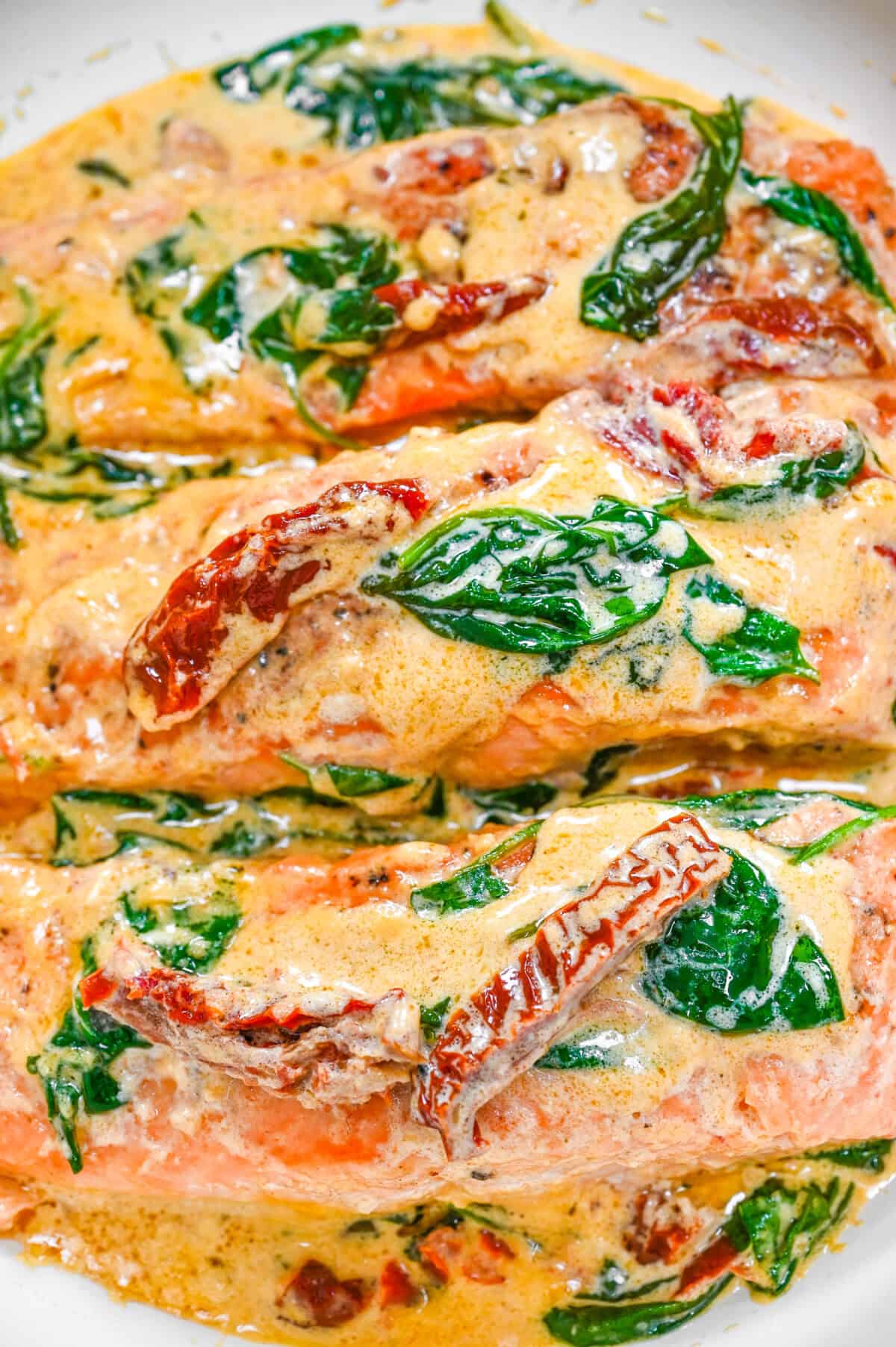 Close-up of creamy Tuscan salmon with sun-dried tomatoes and wilted spinach in a rich garlic Parmesan sauce in a skillet.