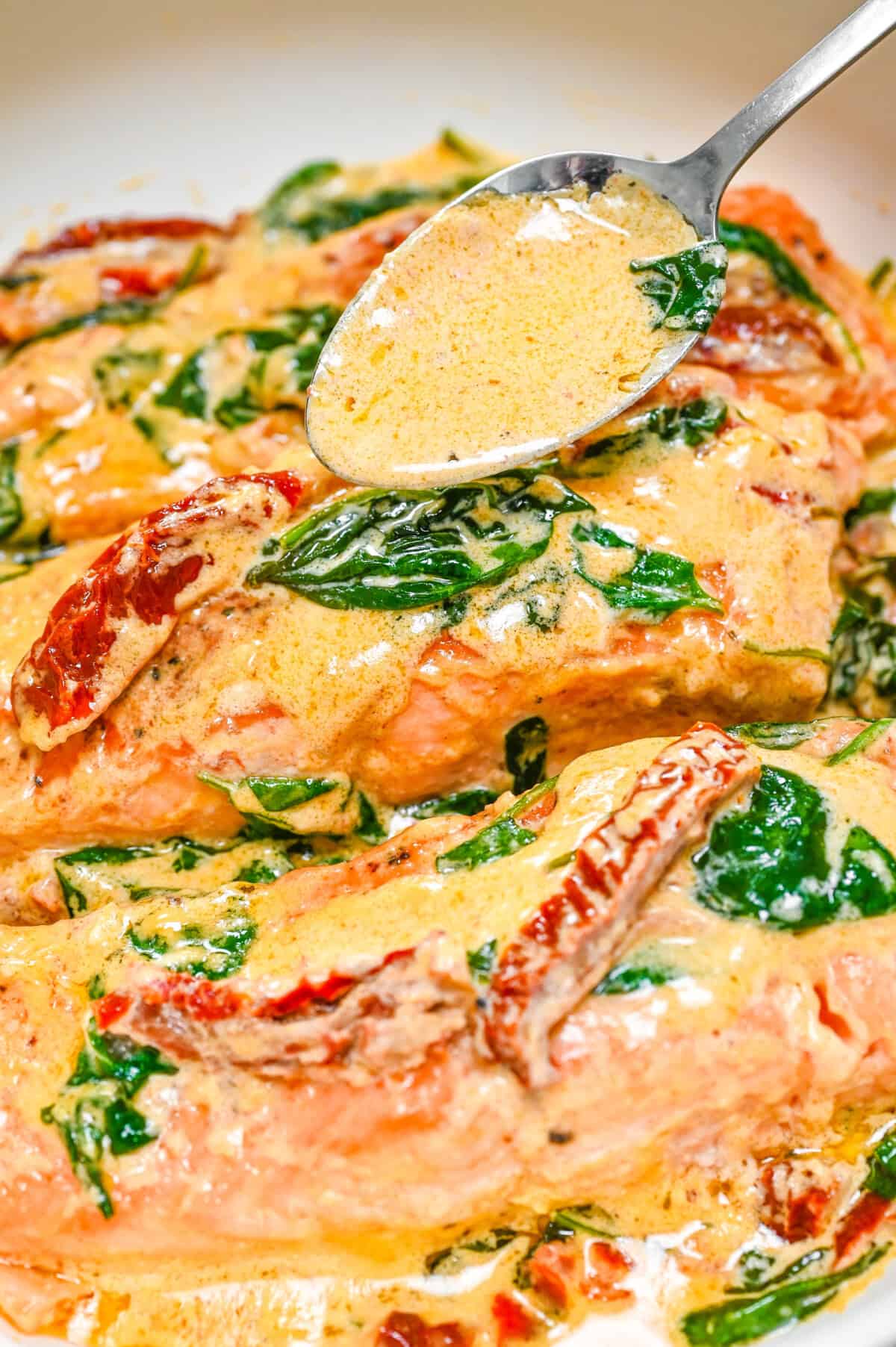 Pan-seared salmon fillets covered in creamy garlic parmesan sauce with spinach and sun-dried tomatoes