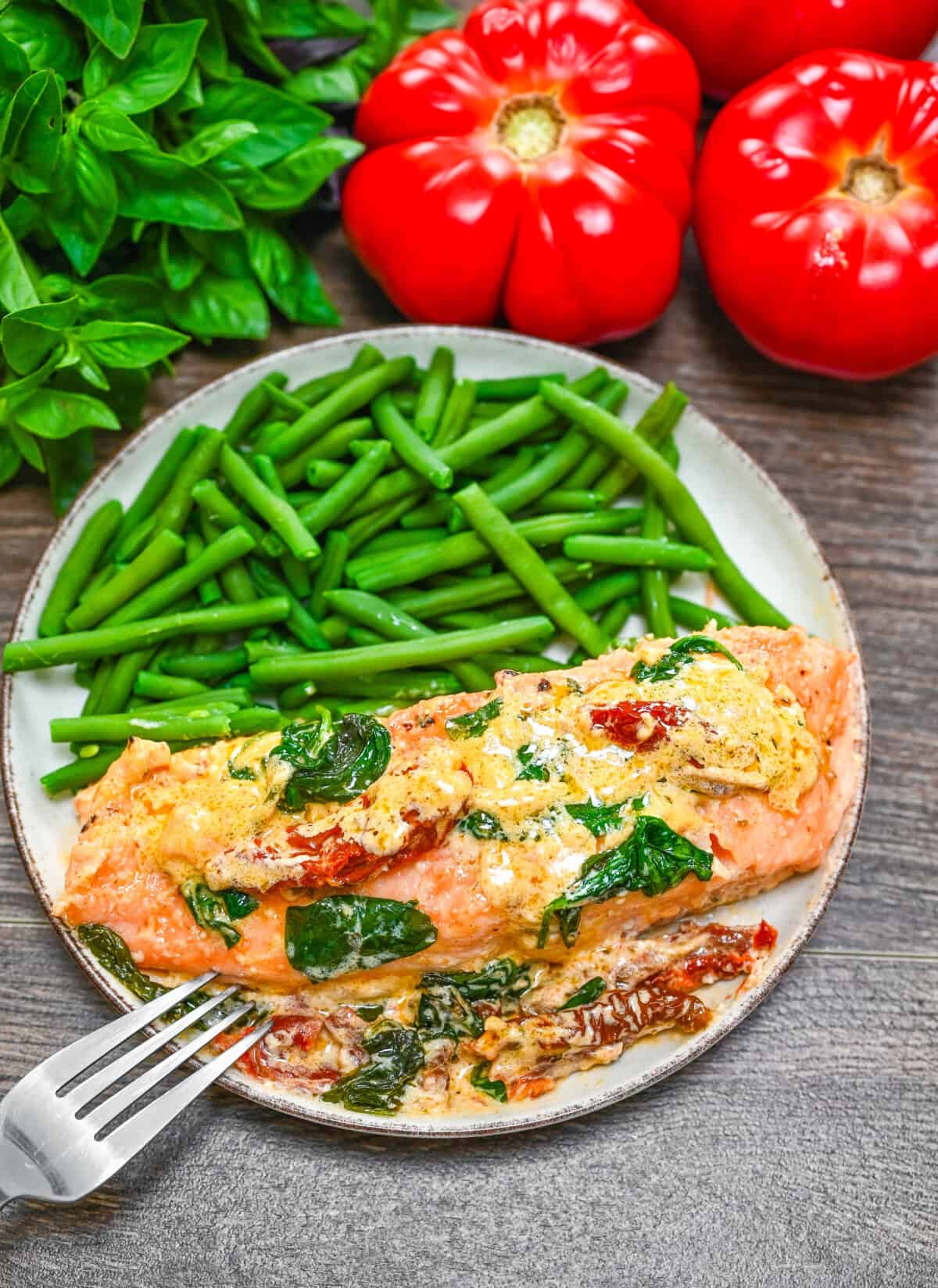A white plate with cooked creamy Tuscan salmon and a side of green beans.