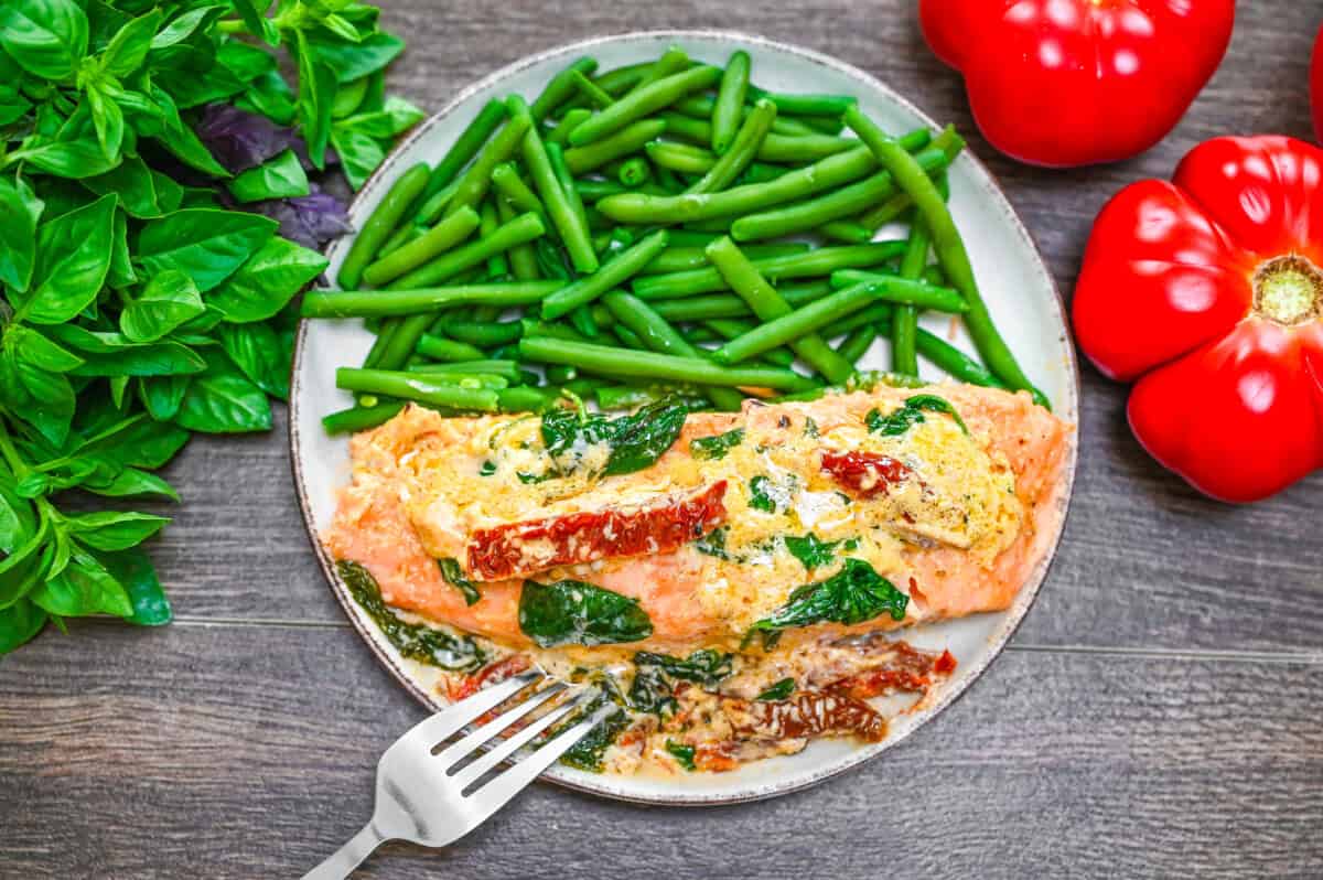Creamy Tuscan salmon served on a plate with green beans, surrounded by fresh basil and tomatoes.