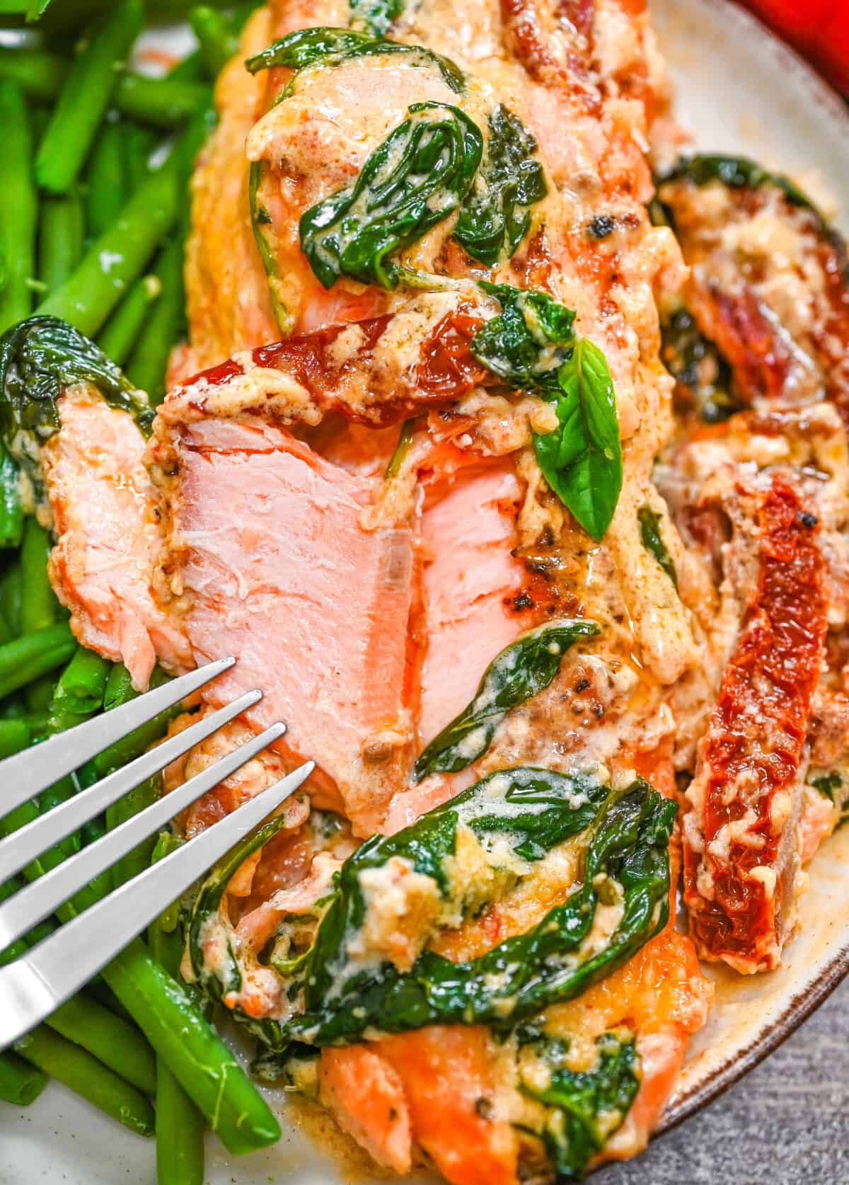 A plate with flackey Tuscan salmon with creamy sauce, spinach and sun-dried tomatoes