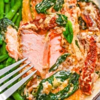 A plate with flackey Tuscan salmon with creamy sauce, spinach and sun-dried tomatoes