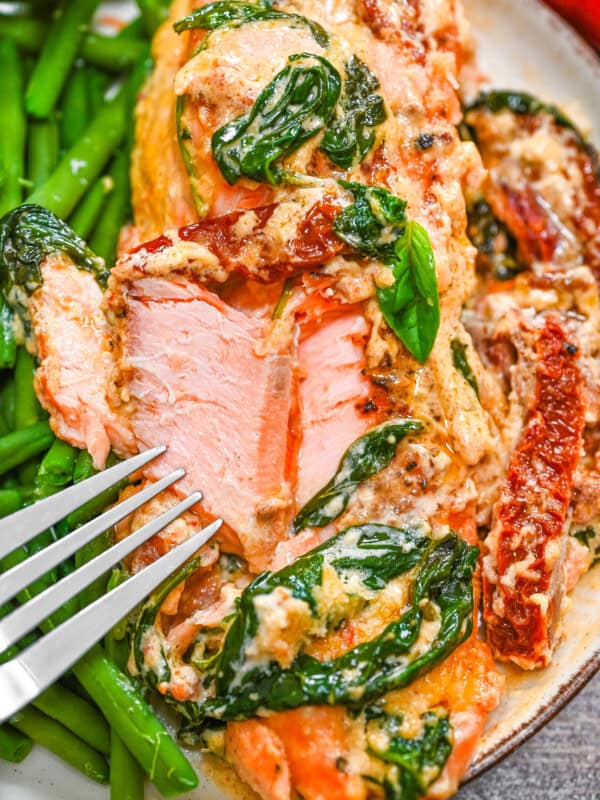 A plate with flackey Tuscan salmon with creamy sauce, spinach and sun-dried tomatoes