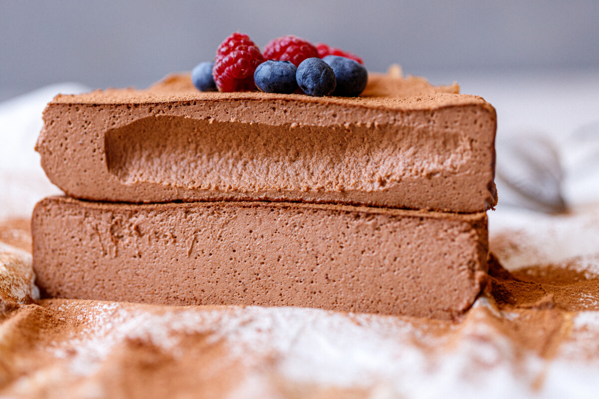 A close-up of a spoonful of chocolate cottage cheesecake in front of the full cake.