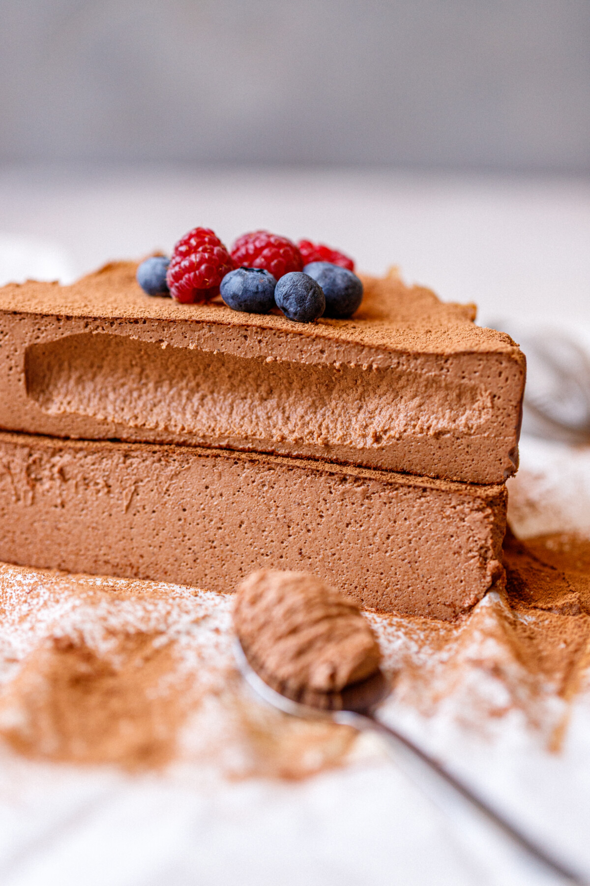 Close-up of a sliced chocolate cottage cheese cheesecake topped with fresh berries and dusted with cocoa powder