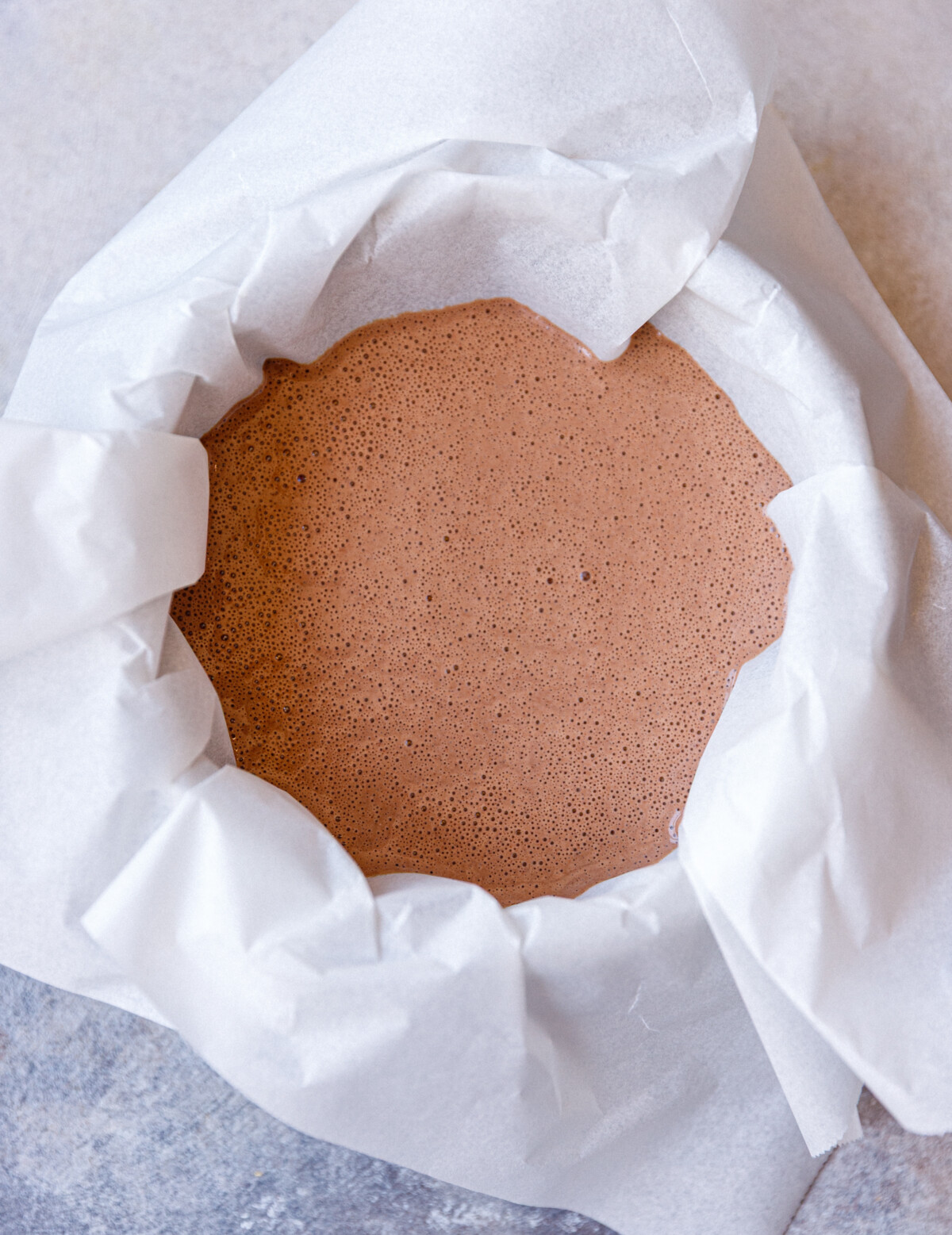 A round 6-inch cake pan lined with parchment paper with mixture for chocolate cottage cheesecake.