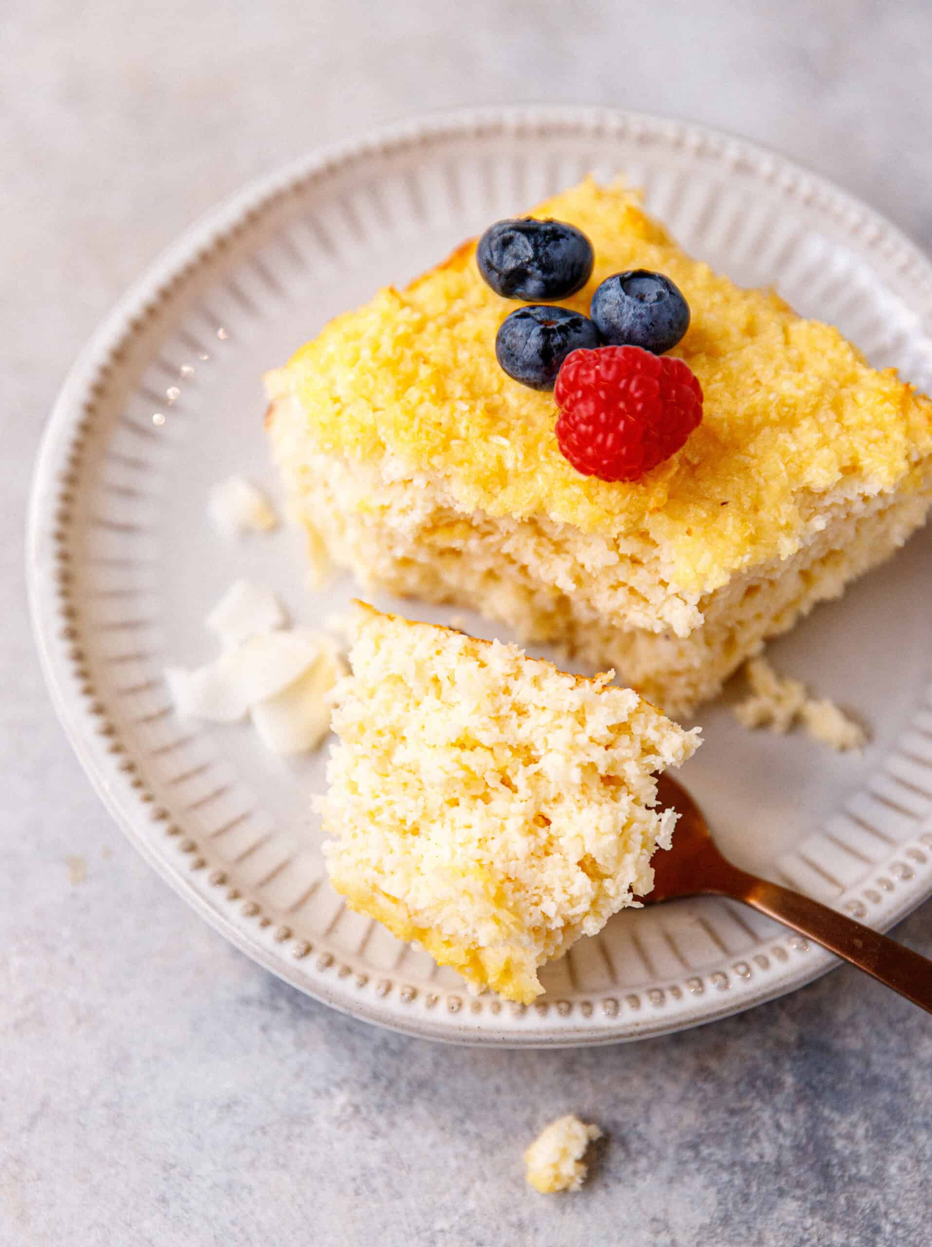 Coconut yogurt cake served on a plate, topped with raspberries and blueberries.