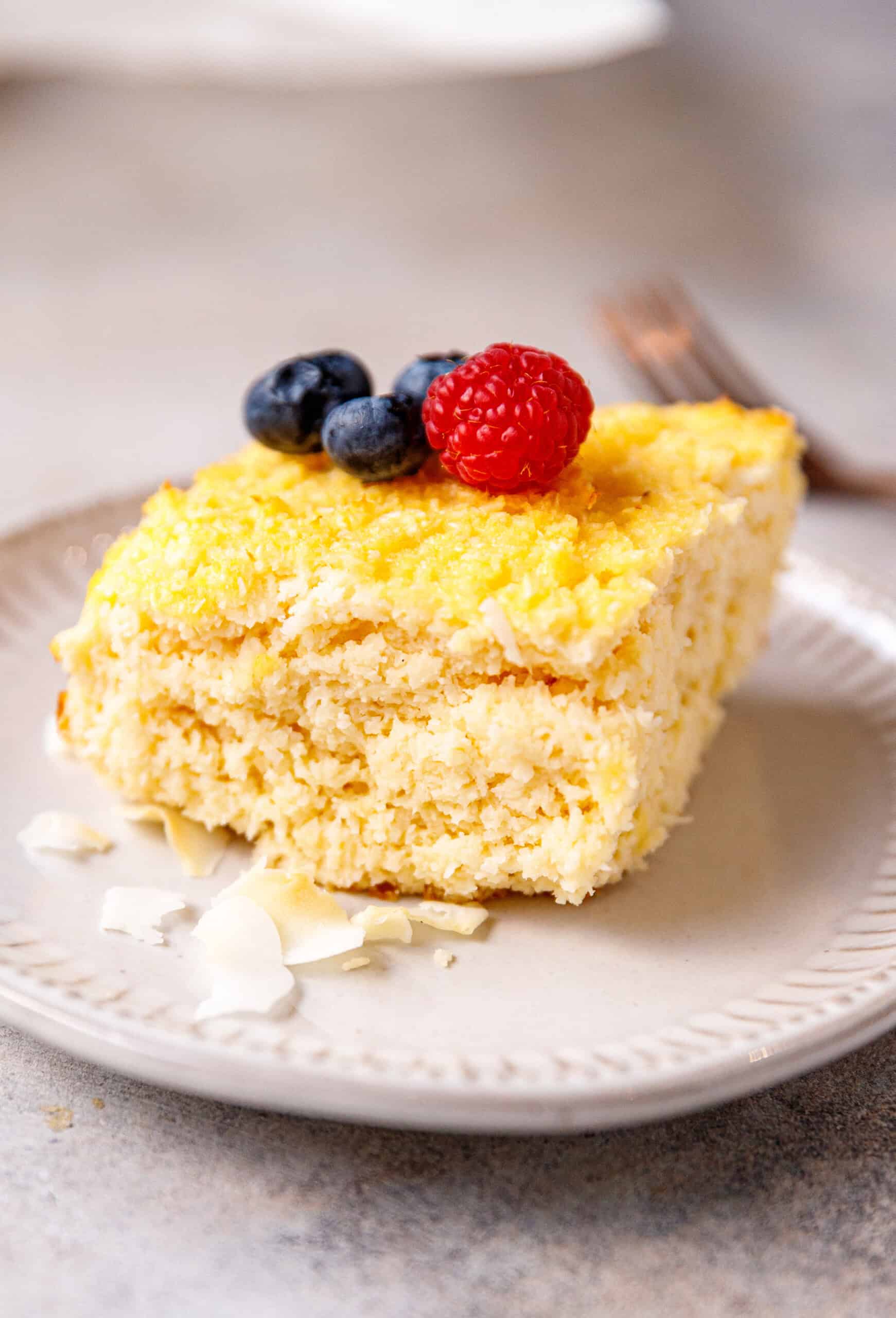 A slice of 6-ingredient yogurt and coconut cake on a plate, topped with berries.