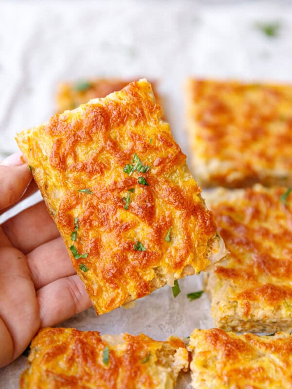 A hand holding a square of cabbage and egg frittata