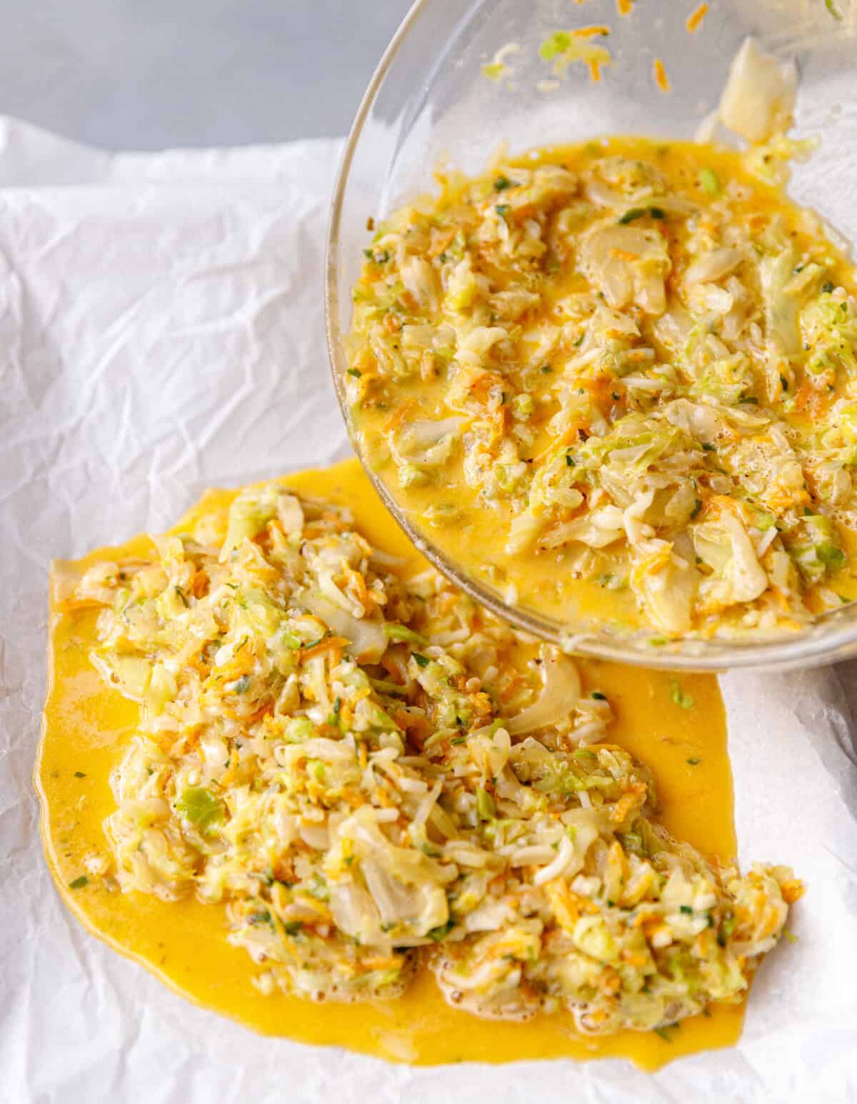 Egg and cabbage bake mixture being poured into a parchment paper lined baking sheet.