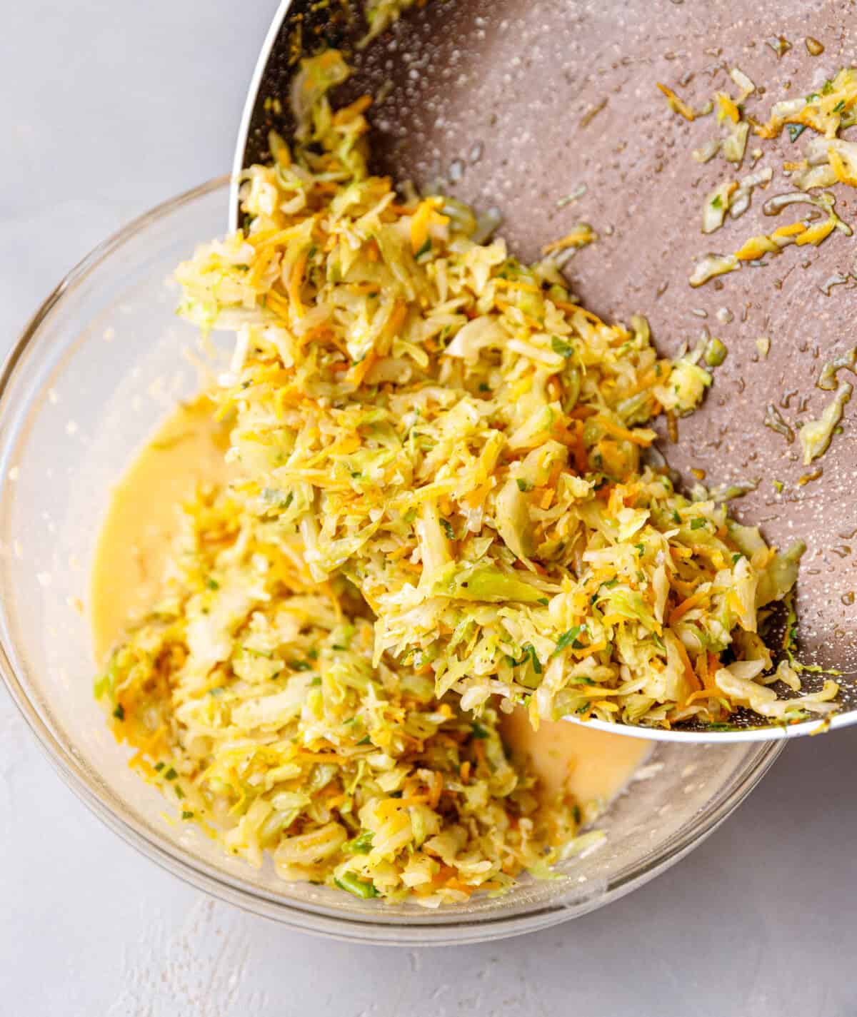 Cooked cabbage and carrot in a pan being combined with a mixture of eggs, milk cheese and flour.