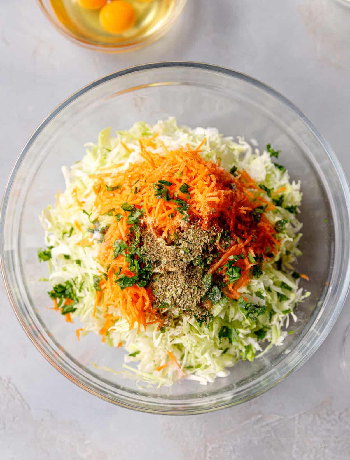 Shredded cabbage, grated carrot, and spices in a glass mixing bowl, ready to make a vegetable frittata.