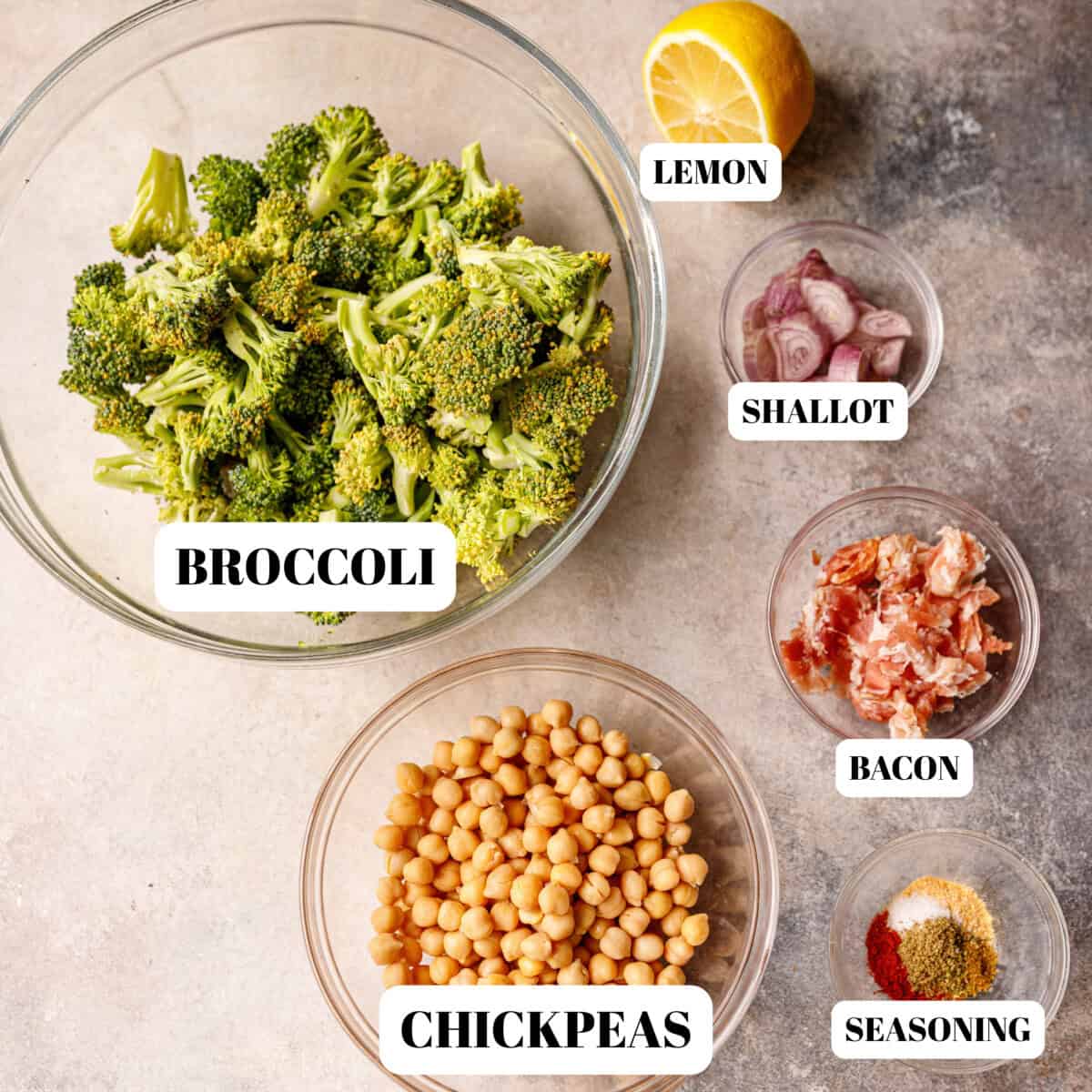 Clear bowls with broccoli, chickpeas, shallots, bacon and seasoning for roasted broccoli salad.
