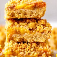 Close-up of gluten-free peach bars with a golden oat–almond crumble and juicy peach filling stacked parchment paper.
