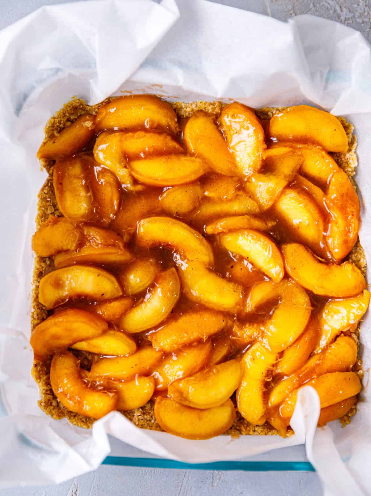 Juicy peach filling spread over the almond oat crust in a square baking dish.