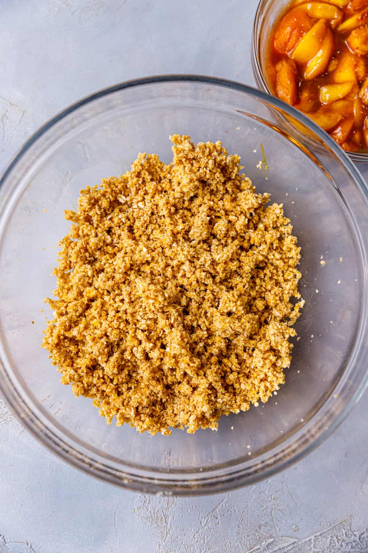 A glass bowl with almond oat crumbs for Peach bars.