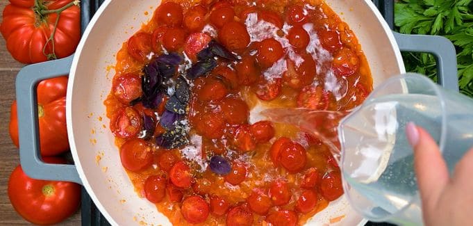 Adding fresh basil and water to tomato base for creamy cheese pasta sauce.