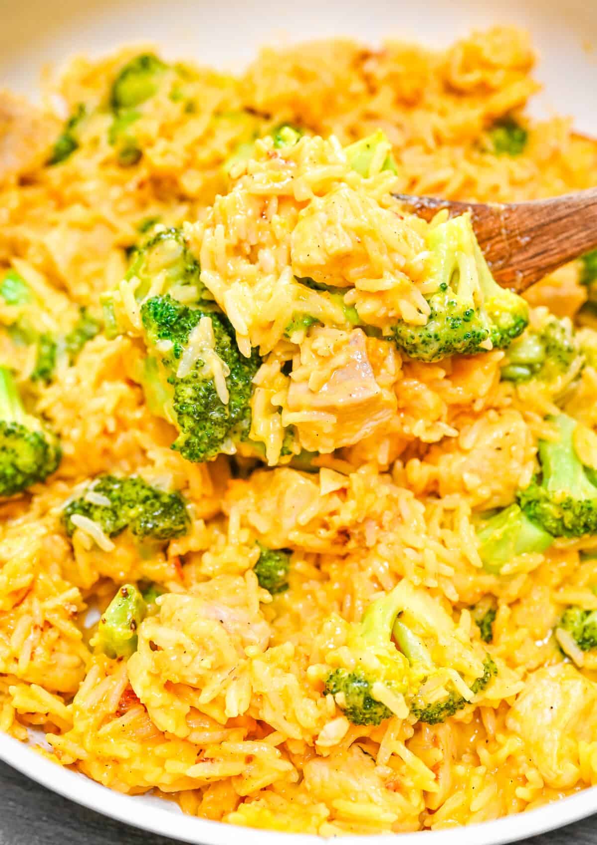 A wooden spoon with rice and broccoli chicken casserole with fresh parsley garnish