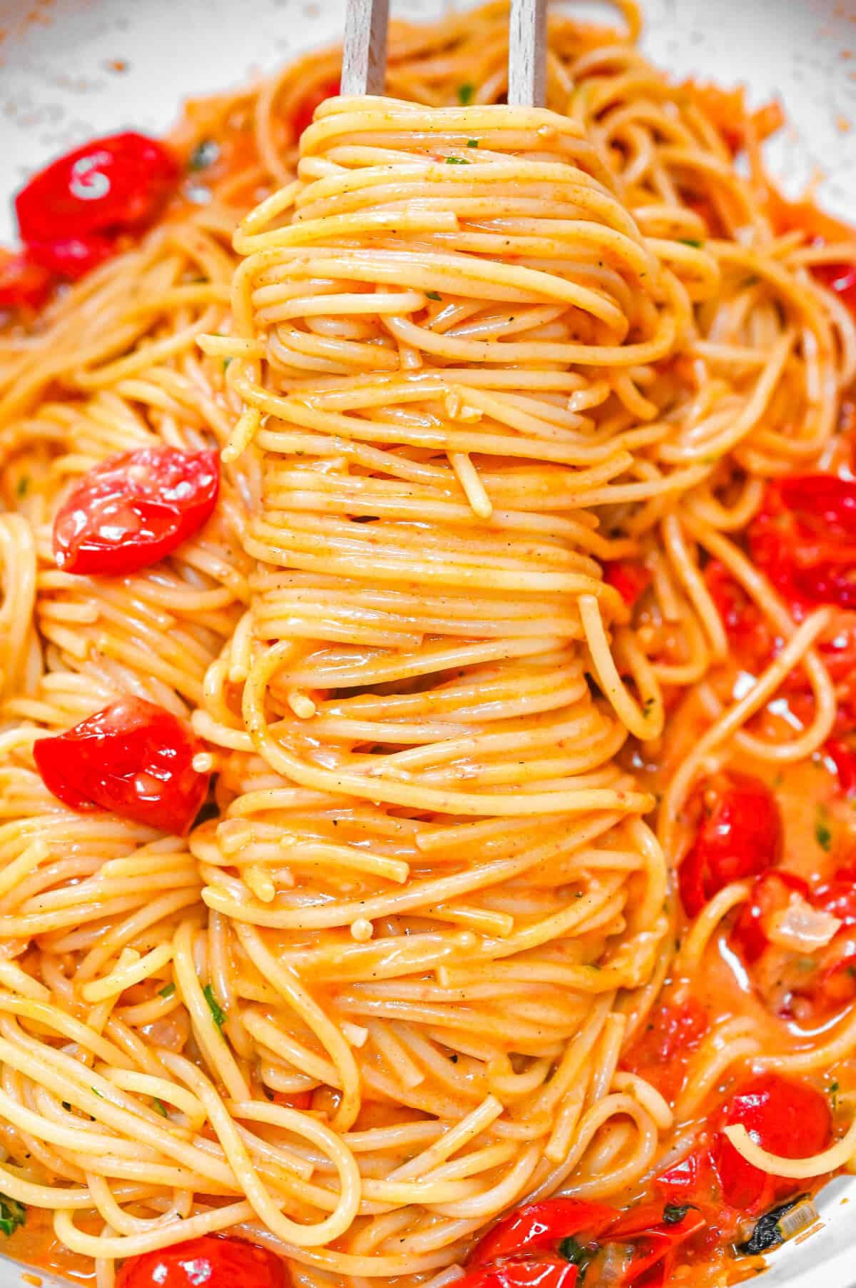 paghetti wrapped around wooden chopsticks, coated in creamy tomato sauce with cherry tomatoes.