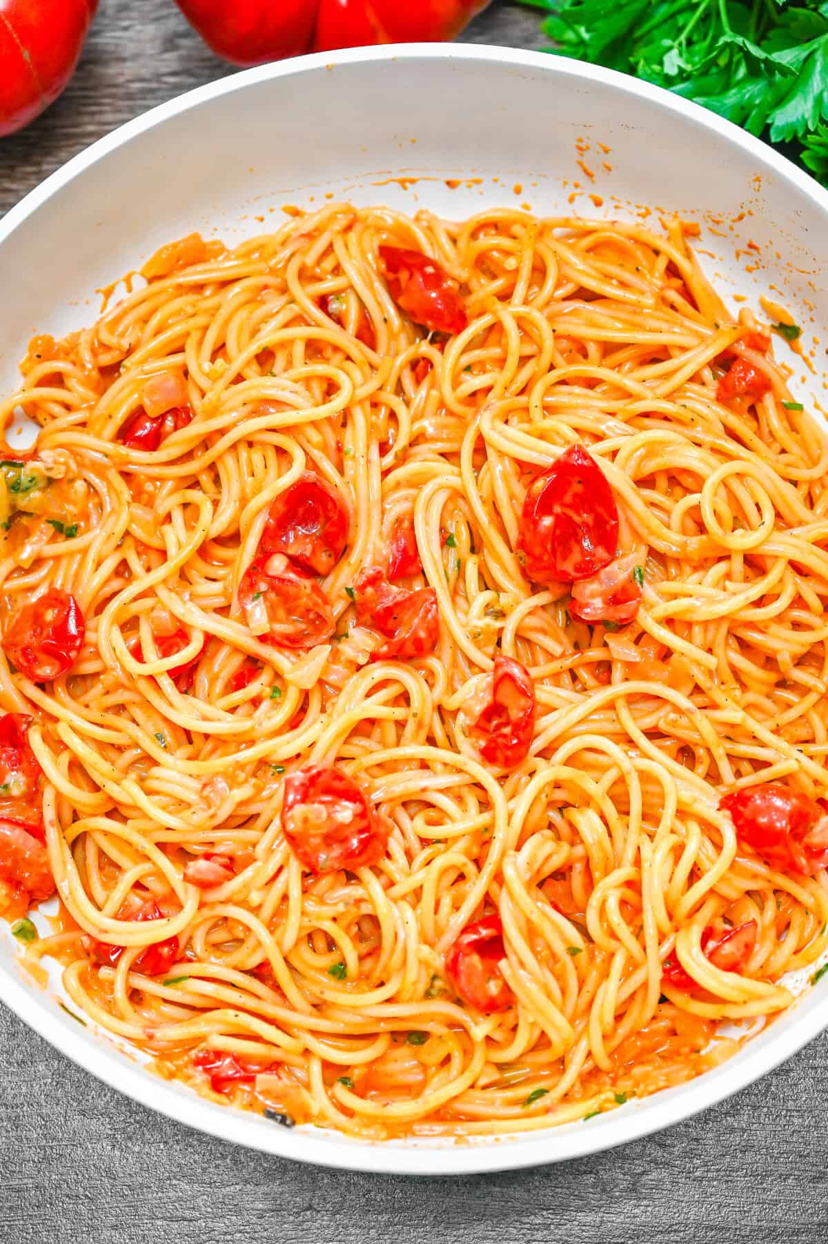 Spaghetti in a white pan with creamy tomato sauce and cherry tomatoes, garnished with herbs.