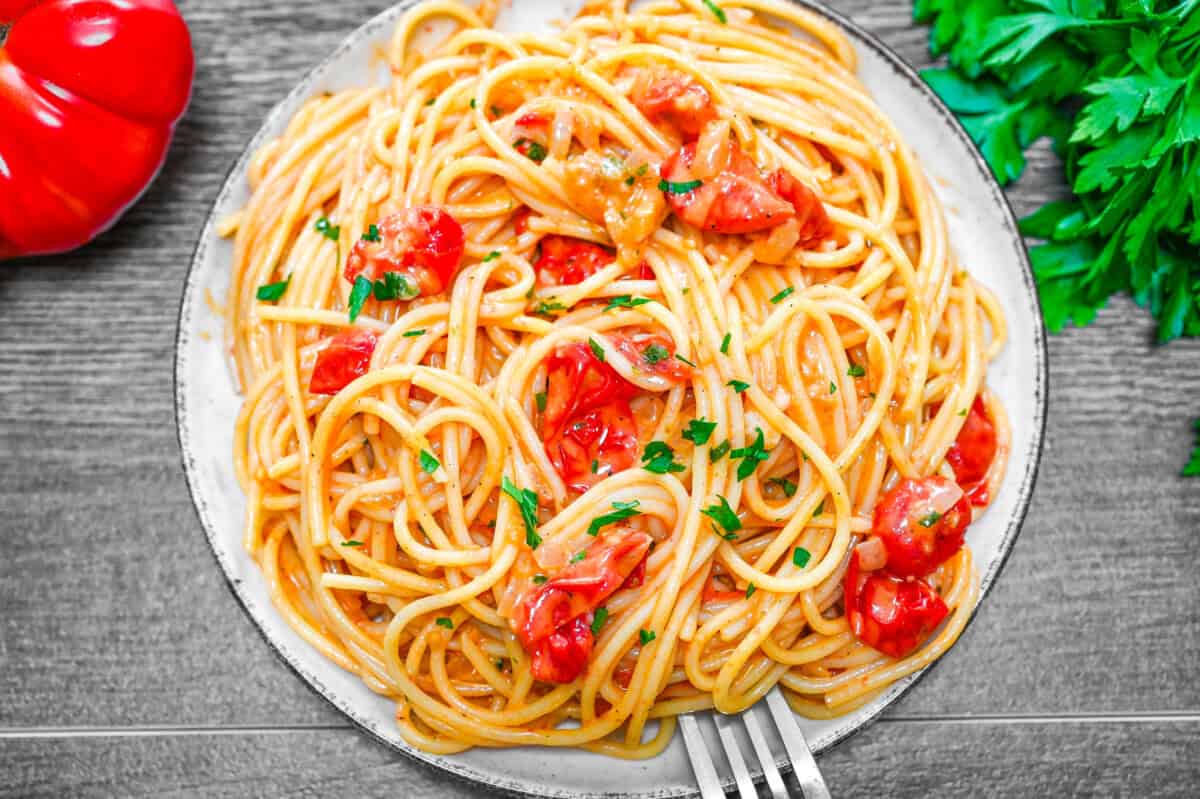 Plate of spaghetti in creamy tomato sauce with cherry tomatoes and fresh parsley, served with a fork.