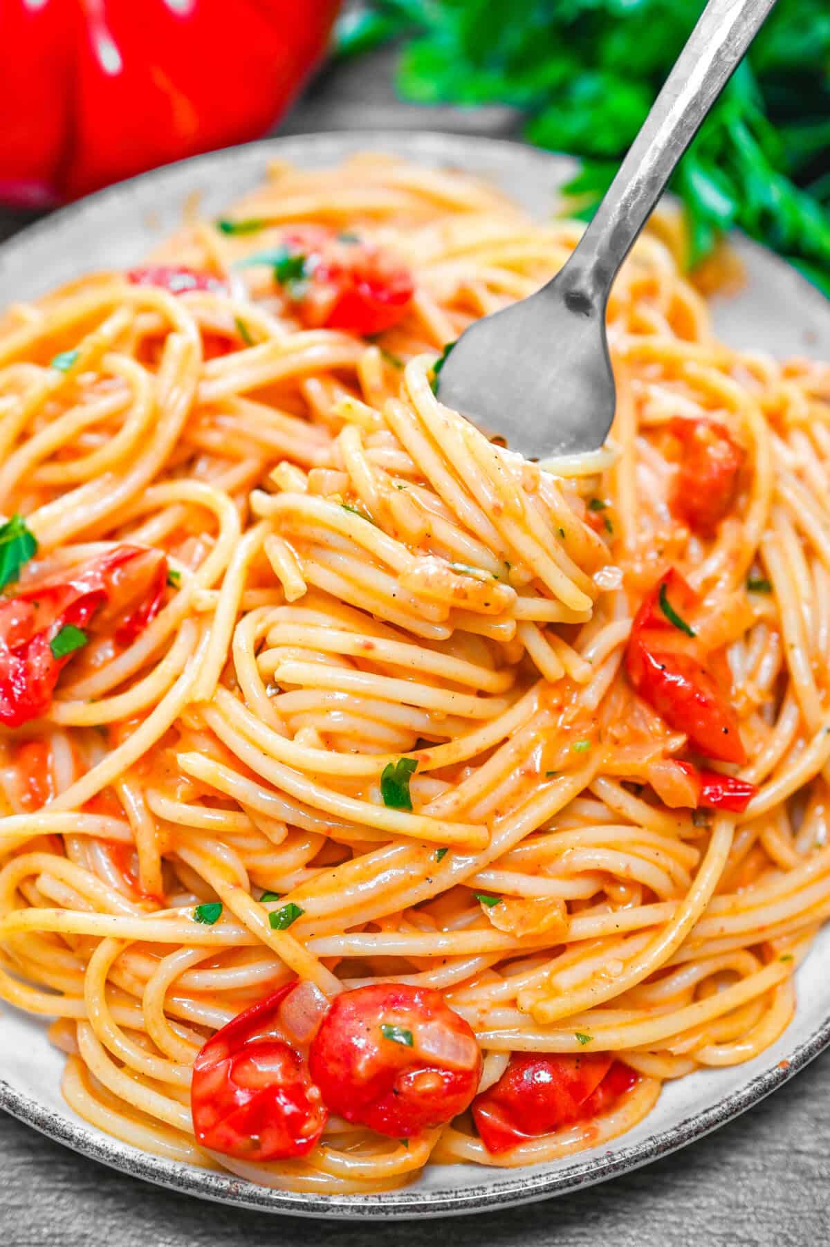 Creamy spaghetti with cherry tomatoes and herbs on a plate, twirled on a fork.