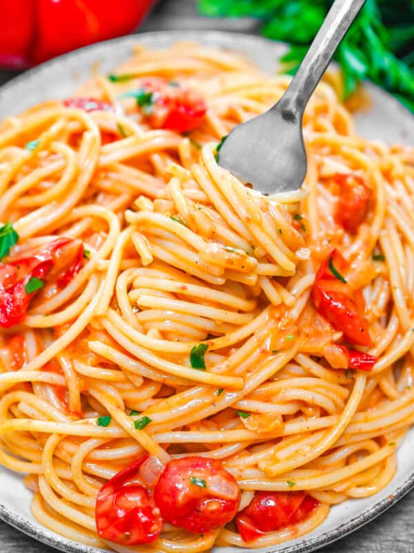 Creamy spaghetti with cherry tomatoes and herbs on a plate, twirled on a fork.