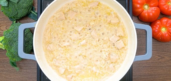 A skillet with chicken, rice, onion, broth and milk.