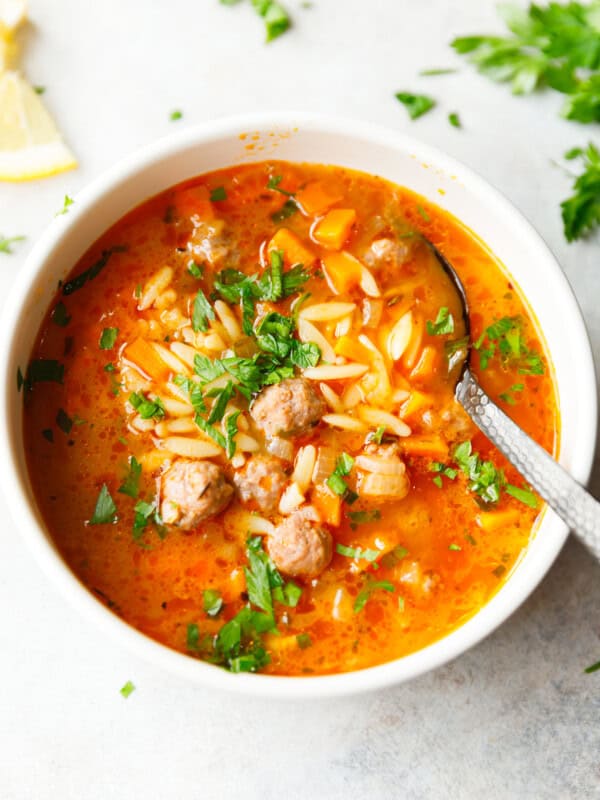 A white bowl with Meatball Orzo Soup topped with Parsley