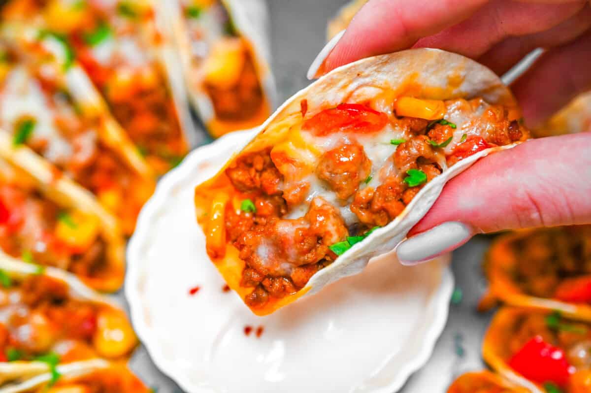 A hand holding mini taco with dipping sauce.