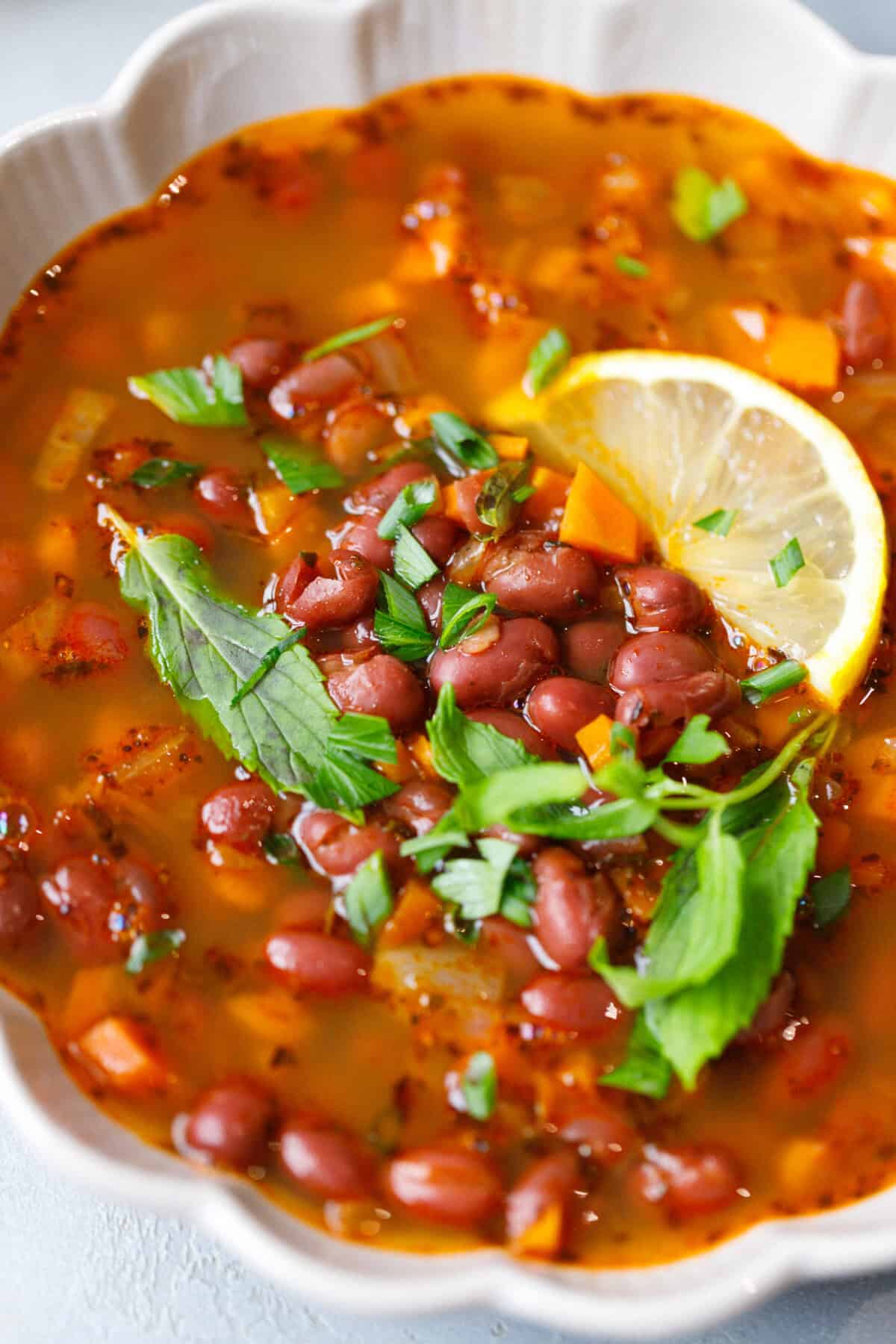 Close-up of canned red bean soup with carrots, herbs, and a slice of lemon in a white bowl — a cozy Bulgarian-style zuppa di fagioli made with olive oil, tomato paste, and fresh herbs.