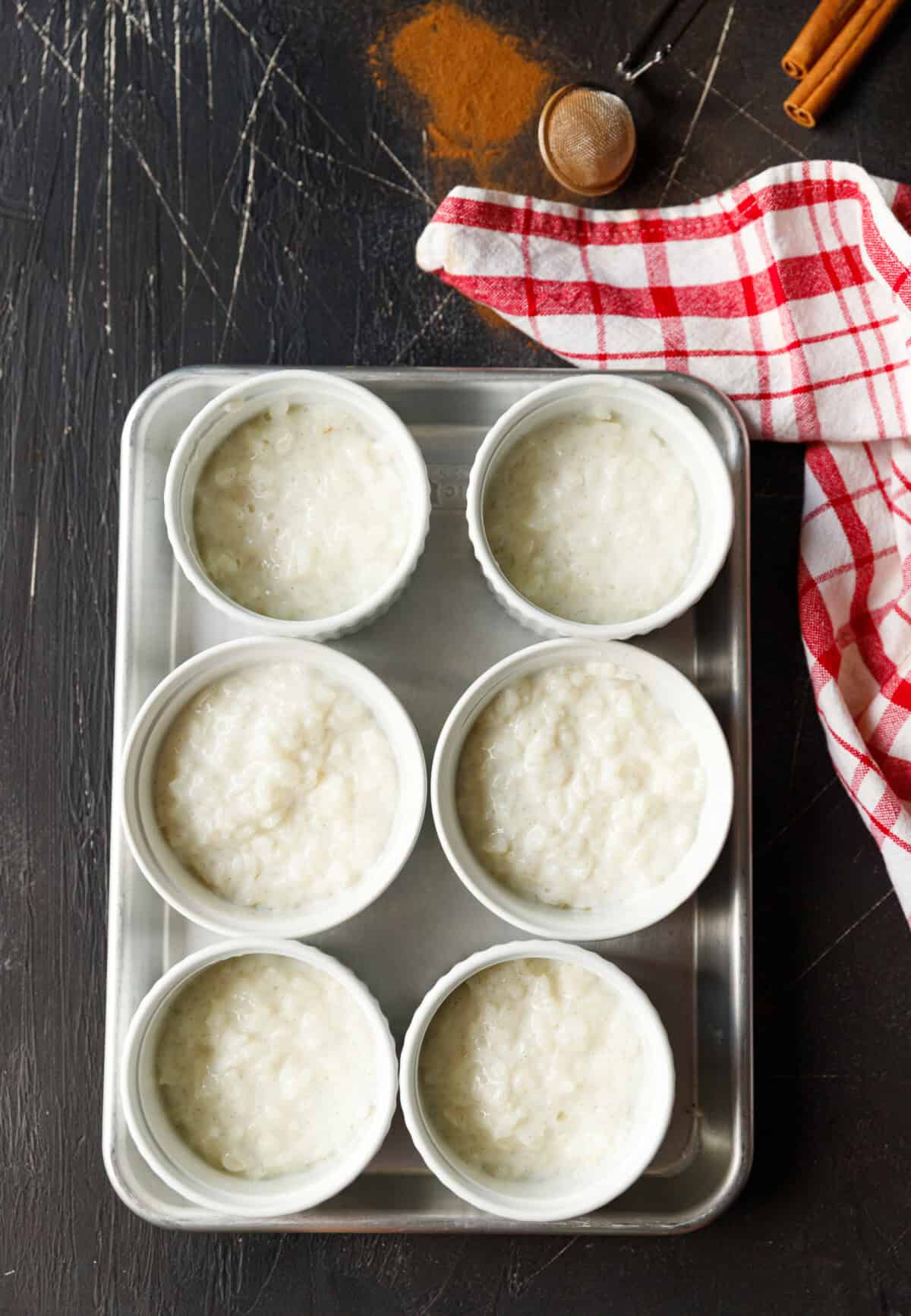 Creamy Bulgarian rice pudding divided into white ramekins, ready to chill or serve, with cinnamon and a red checkered towel on the side.