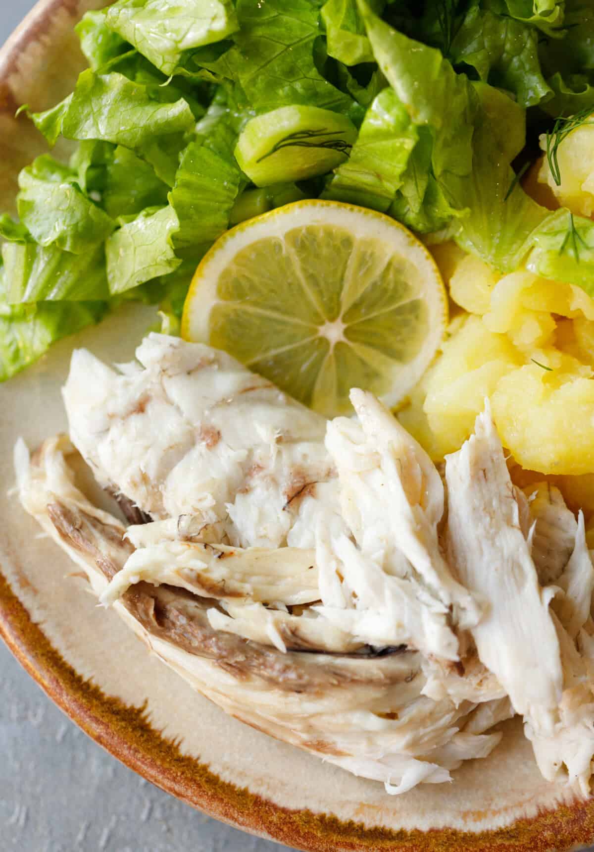 Close-up of flaked roasted milokopi fish served with boiled potatoes, lettuce, and a lemon slice.