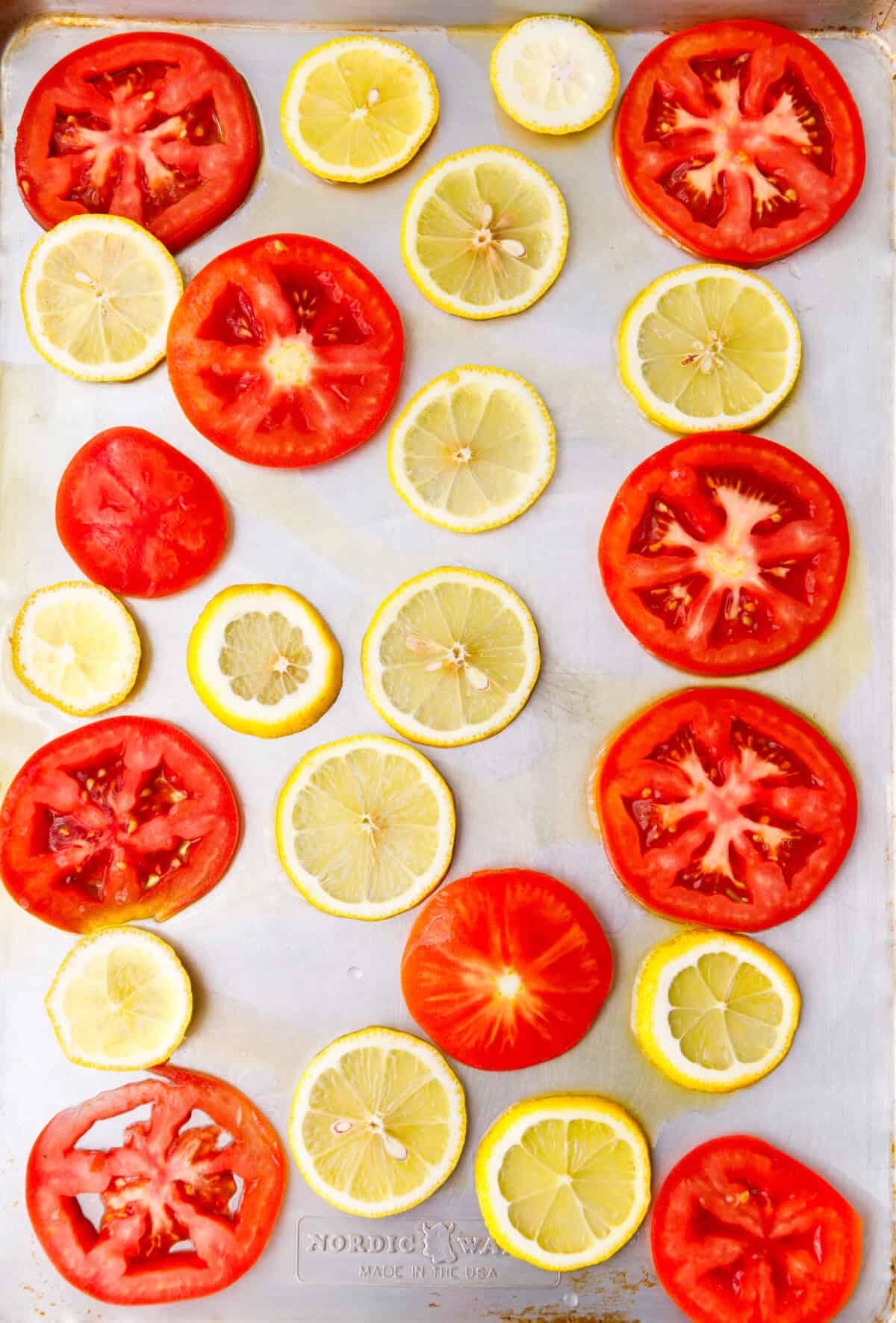 Tomato slices and lemon slices arranged on a baking sheet as a base for baking fish.