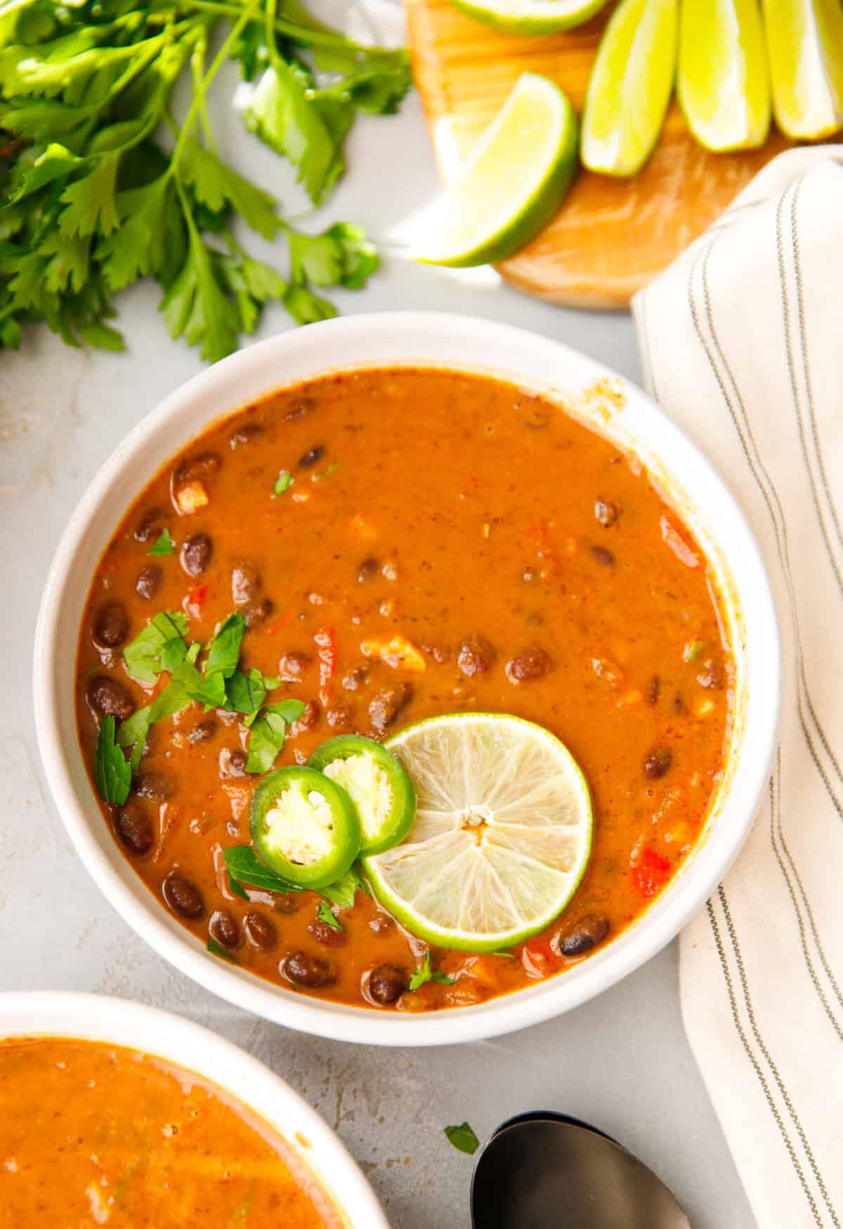 Bowl of creamy black bean soup topped with sliced lime, jalapeño, and fresh parsley.